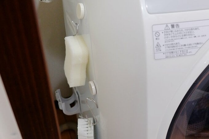 浴室掃除グッズを洗濯機と壁の間につり下げて収納している様子