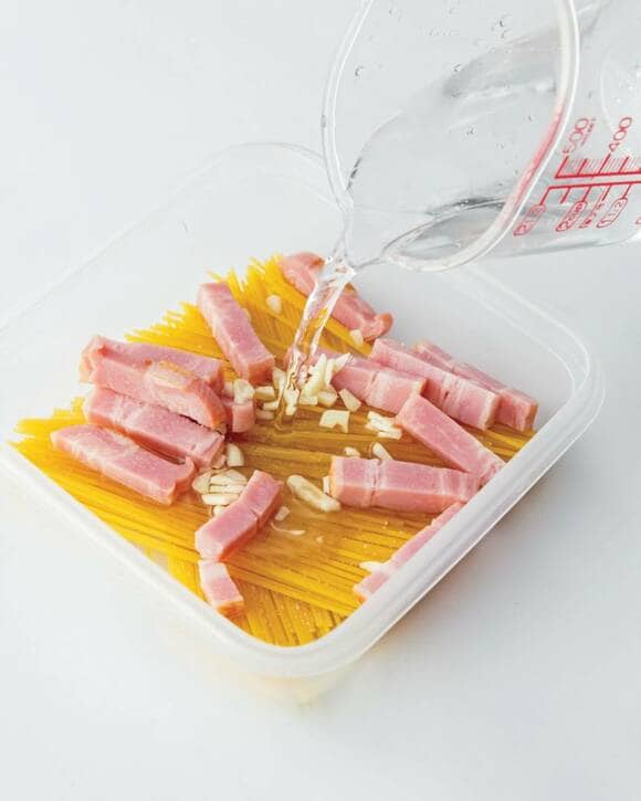 耐熱容器に入っている乾麺とベーコンとニンニクに水を入れる