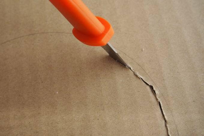 段ボールにカッターで穴をあける様子