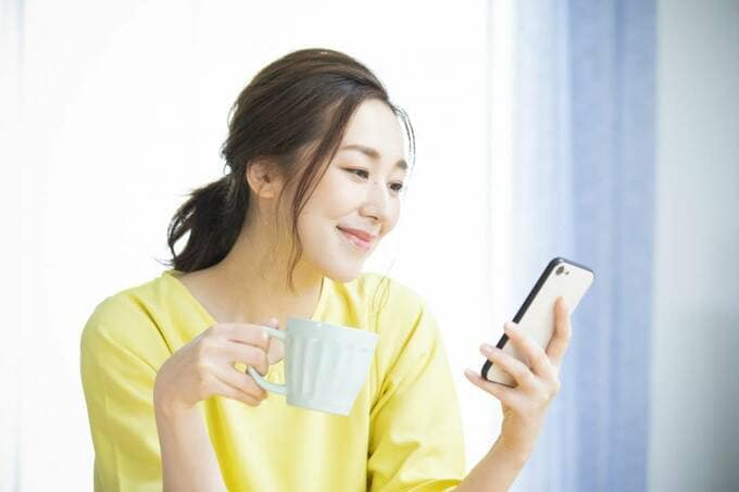 コップを持ちながらスマホを見る女性