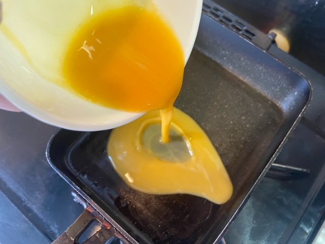 卵焼き器に溶き卵を注ぐ様子