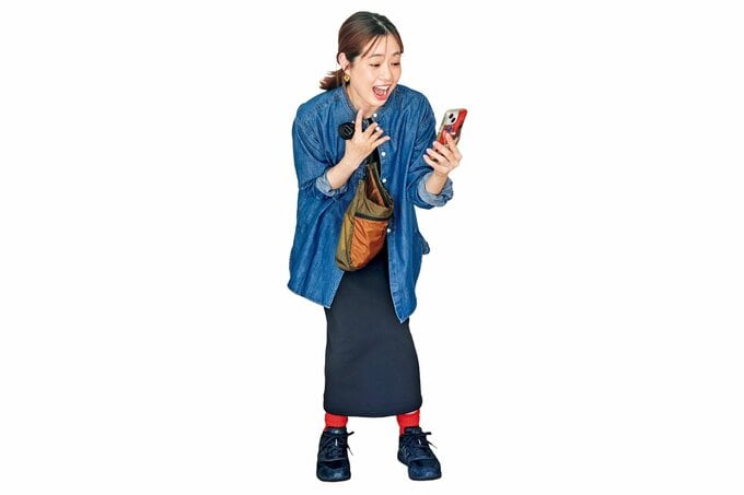 スマホ画面を見ながら「わーっ」と驚いた様子のデニムシャツの女性