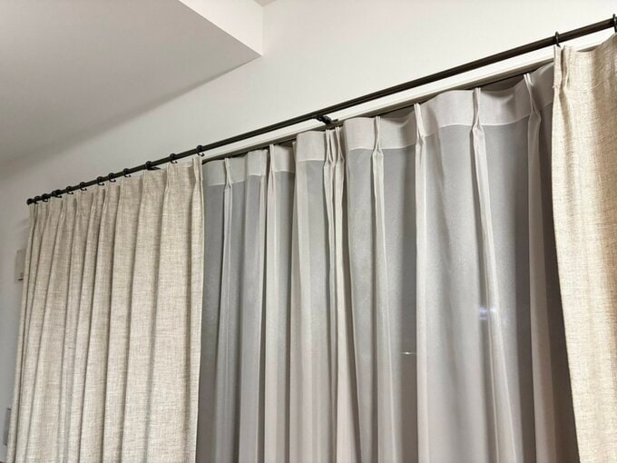 黒いレールにかかったベージュのカーテンが少し開いている窓