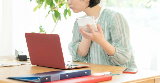 パソコンの前で電卓を持つ女性