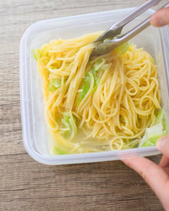 コンテナのパスタをトングでつかむ様子