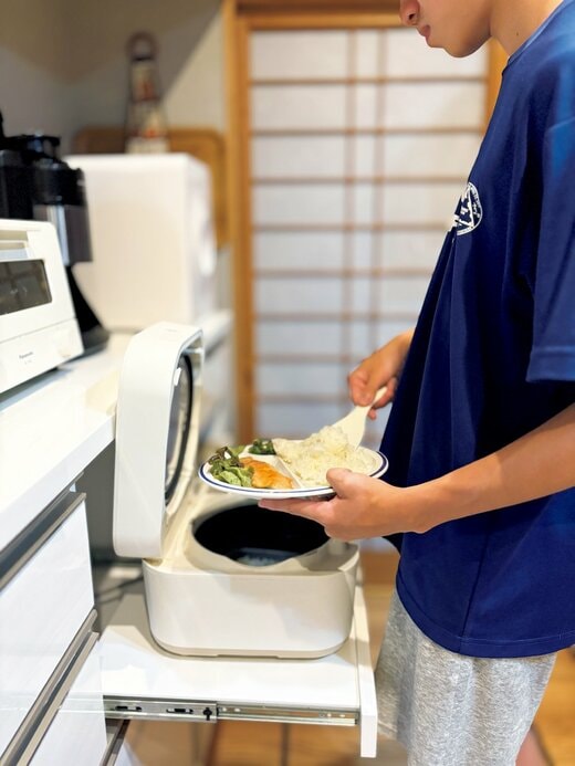 おかずが乗った皿にごはんを盛り付けている若い男性