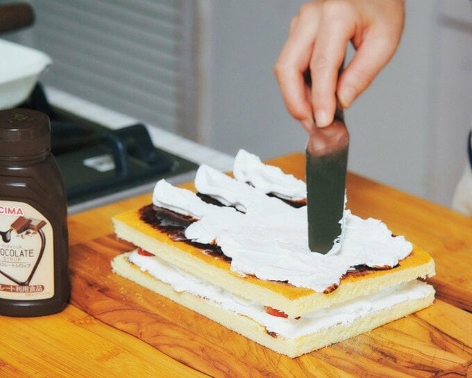 スポンジにチョコレートシロップとホイップクリームを重ねる様子