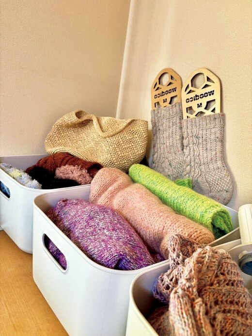 手編みの靴下やストールなどが白いかごに収納されている様子