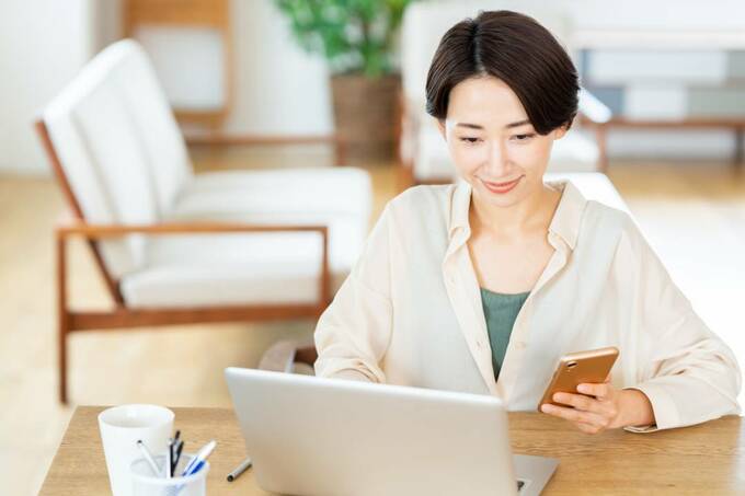パソコンの前にスマホを持つ女性
