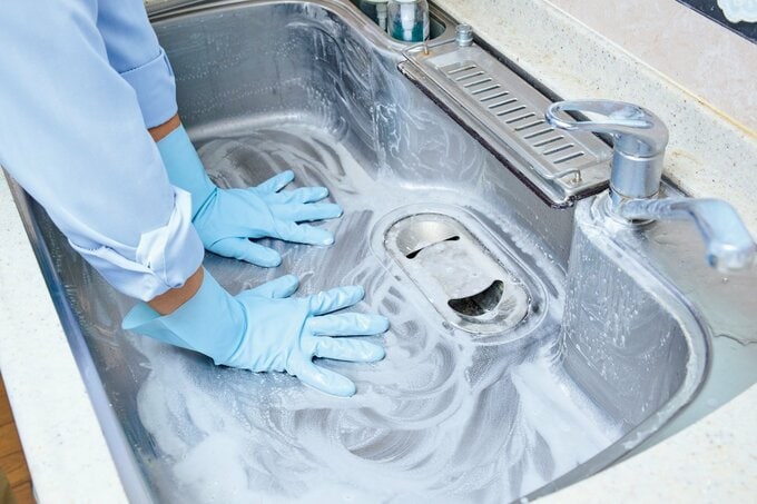 ゴム手袋をはめた両手でシンク全体をクレンザーで磨いている様子
